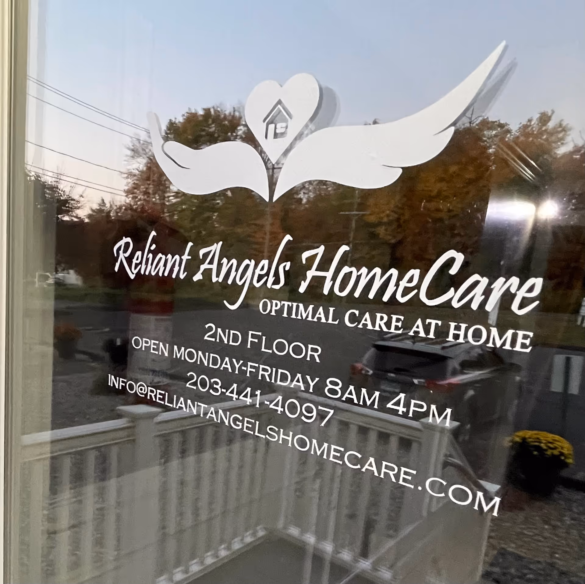 Glass storefront window displaying Reliant Angels HomeCare logo and contact details with reflections.