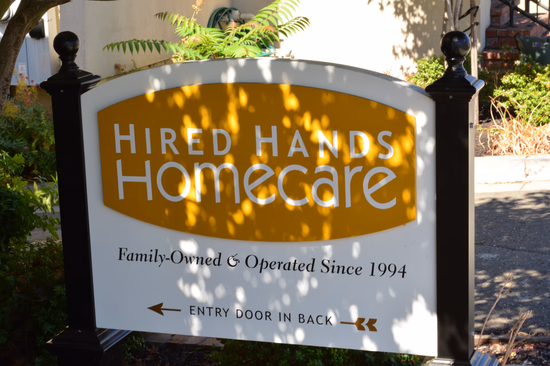 Exterior sign for Hired Hands Homecare with a yellow board and surrounding plants