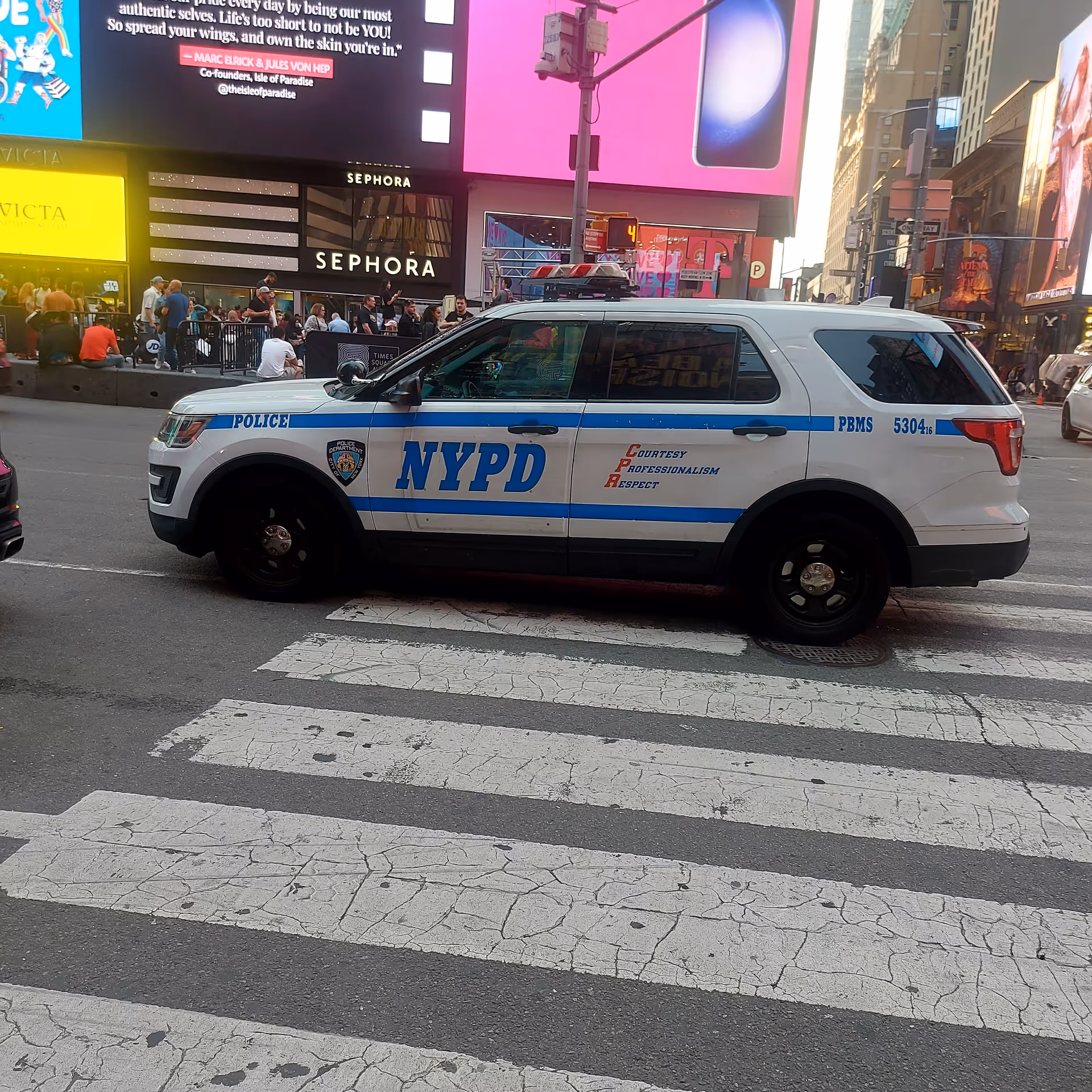 NYPD police SUV parked on a crosswalk in Times Square with bright billboards.