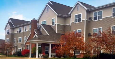 Multi-story senior living facility exterior with a covered entrance and autumn trees.