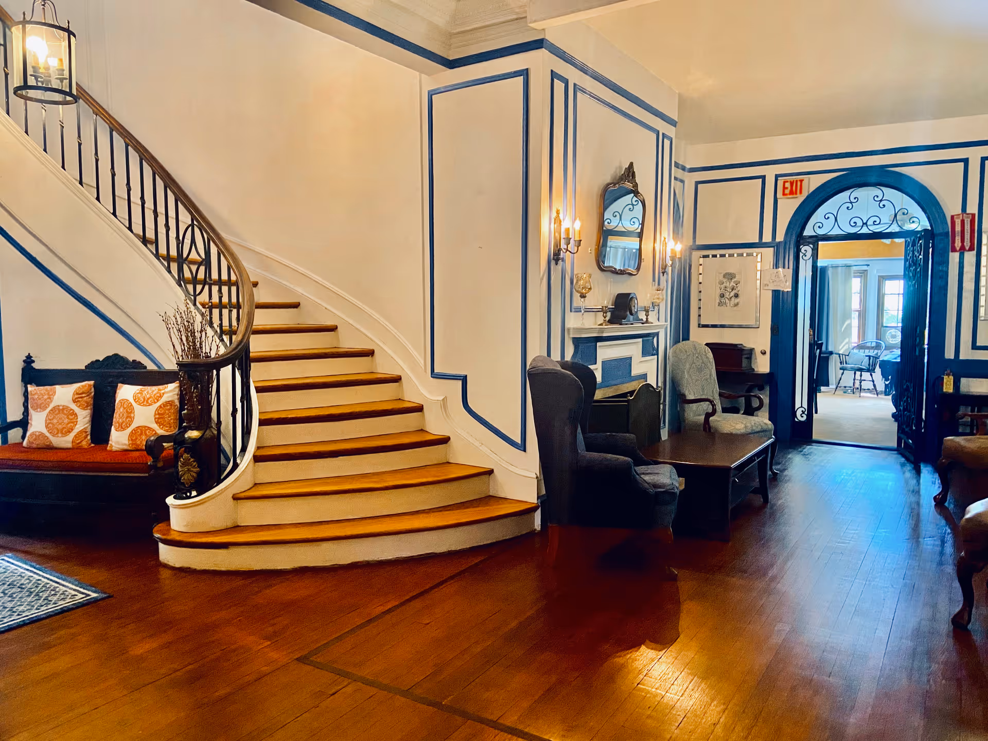 Elegant warm lobby with curved staircase, seating, and blue trim in a senior living facility.
