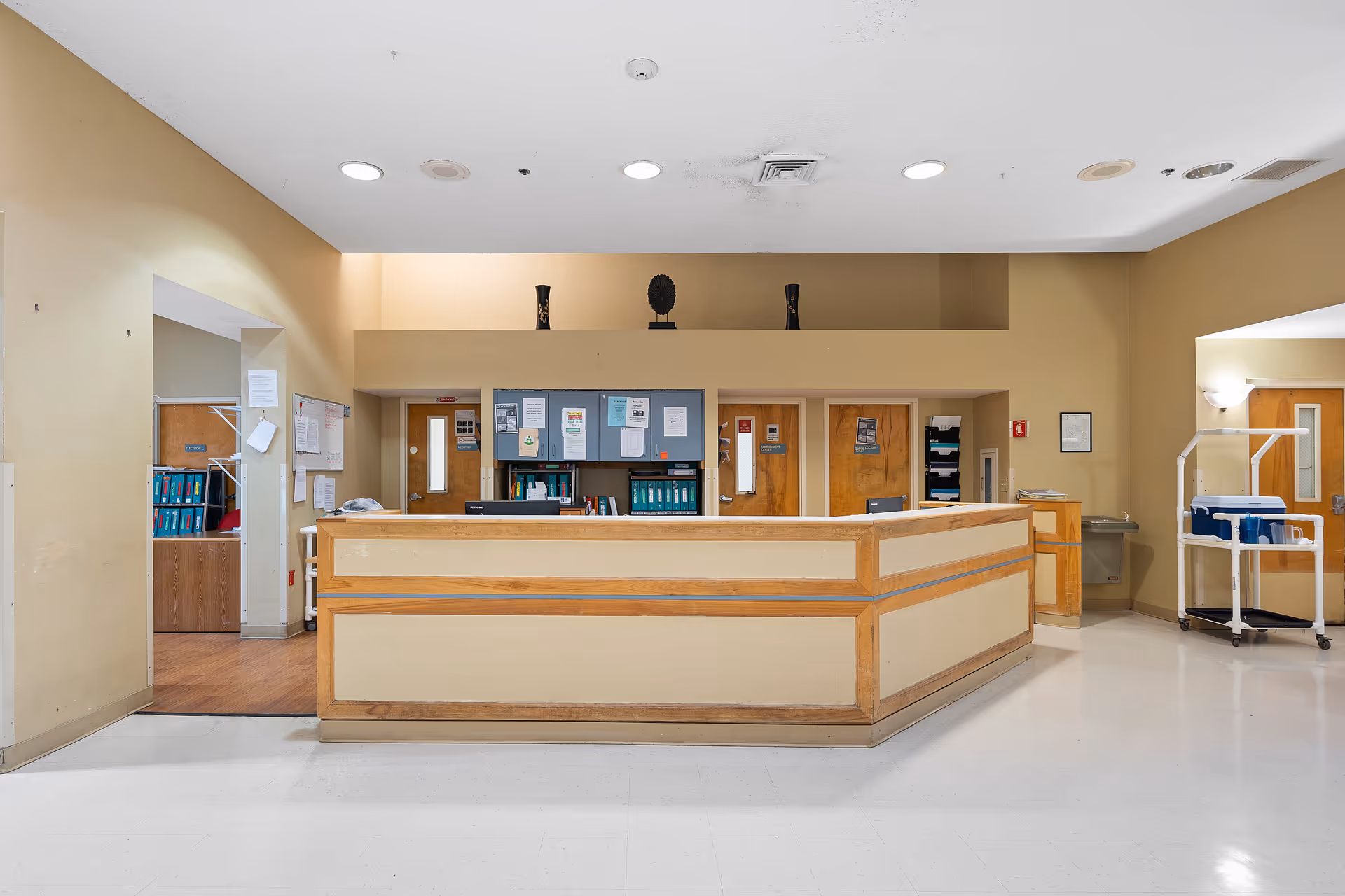 Beige, well-lit interior featuring a wooden front desk in a senior living facility lobby.