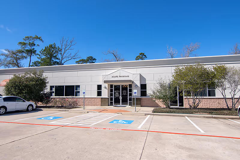 Exterior view of Agape Physicians clinic with parking lot and blue sky.
