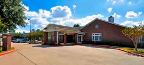 Brick senior living facility with covered entrance, driveway, and manicured landscaping.