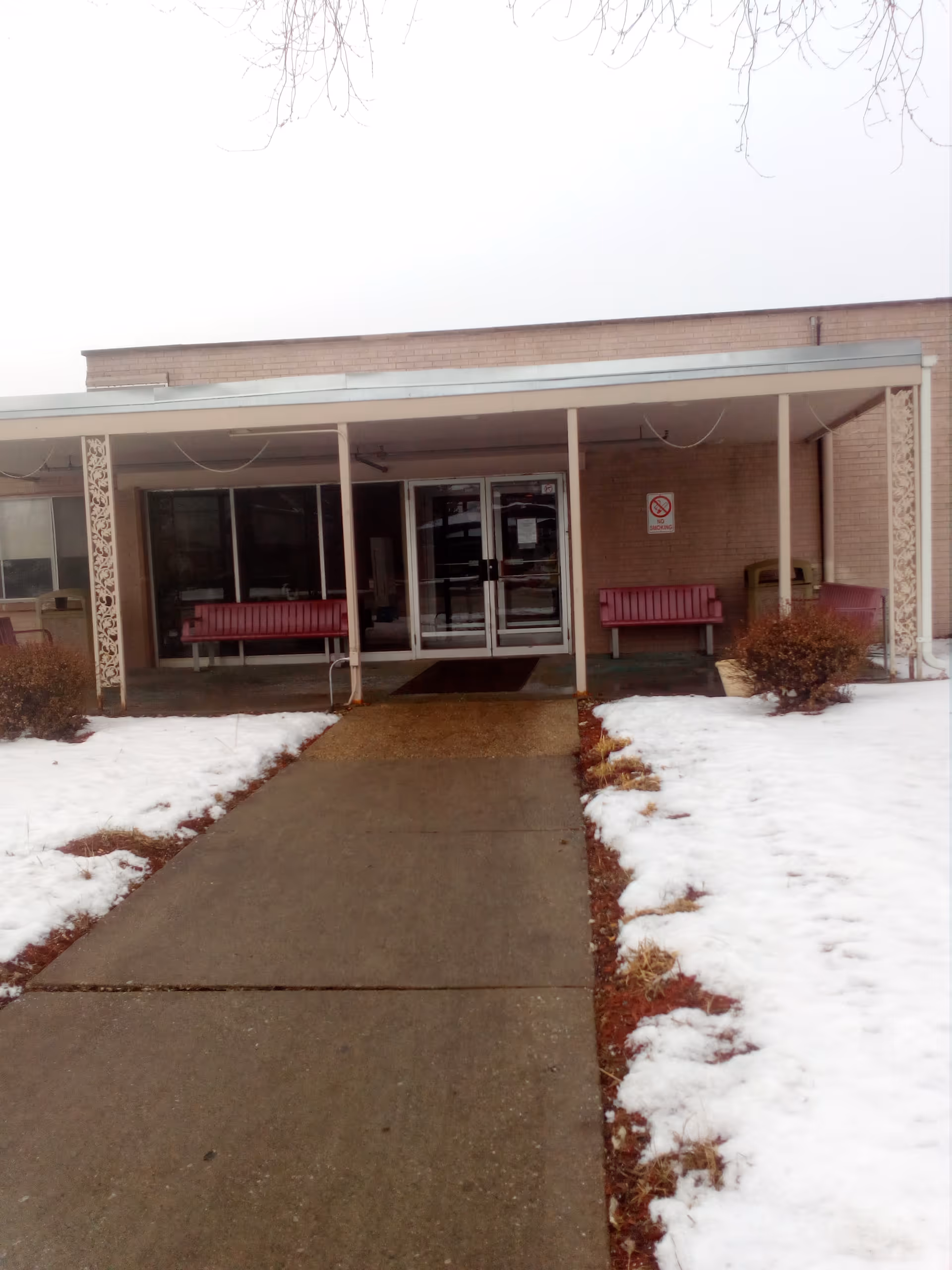 Front entrance of Bria of Palos Hills with glass doors, pink benches, and snow.