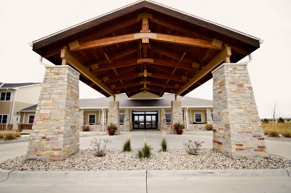 The front entrance of a senior living facility with stone pillars and a wooden porte-cochère.