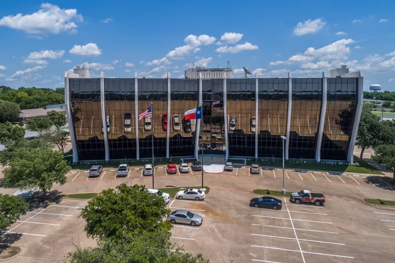 Aerial view of a glass-front building with a parking lot and flags.