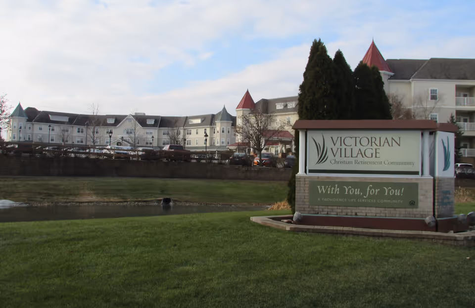 A large Victorian Village sign sits before a multi-building senior living campus.