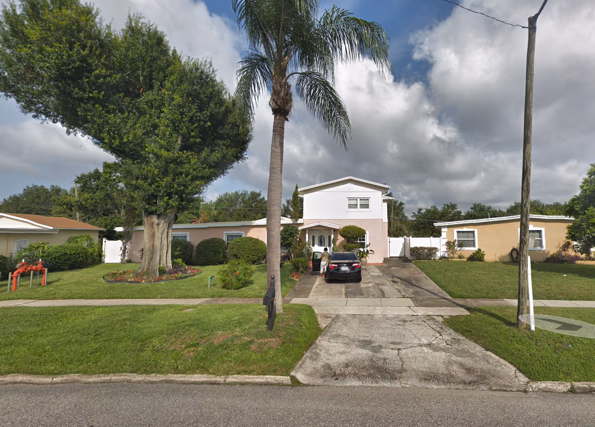Front exterior view of a single-story senior living facility with a driveway and palm trees.