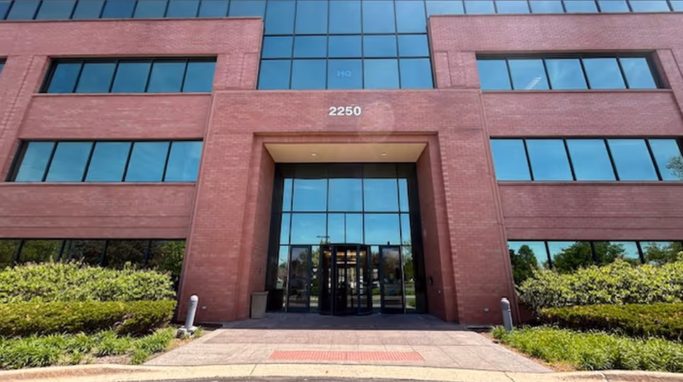 Red brick building entrance with glass doors and surrounding landscaping.