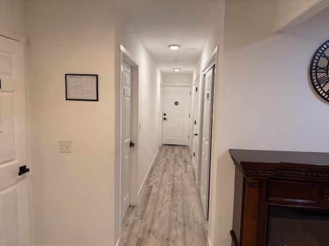 Bright interior hallway with white walls, multiple doors, and a wooden fireplace mantel.