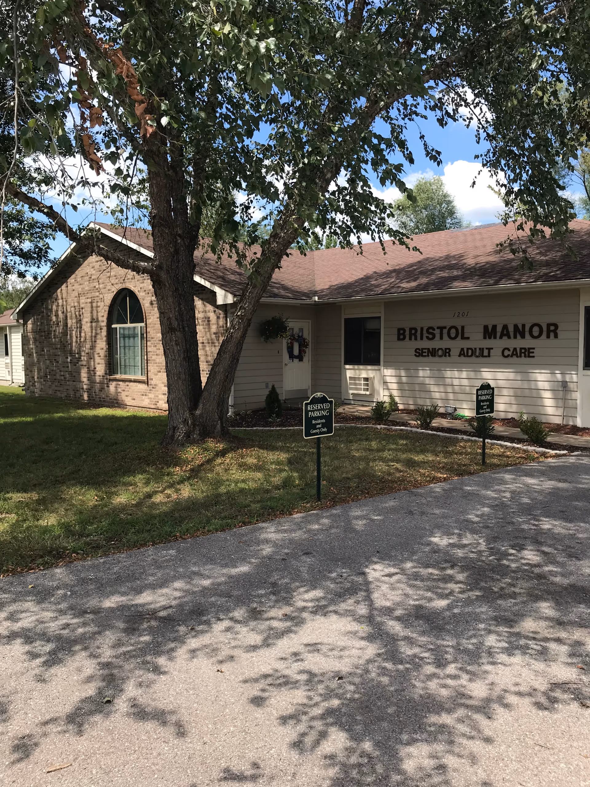Exterior view of Bristol Manor Eldon building with trees and parking.