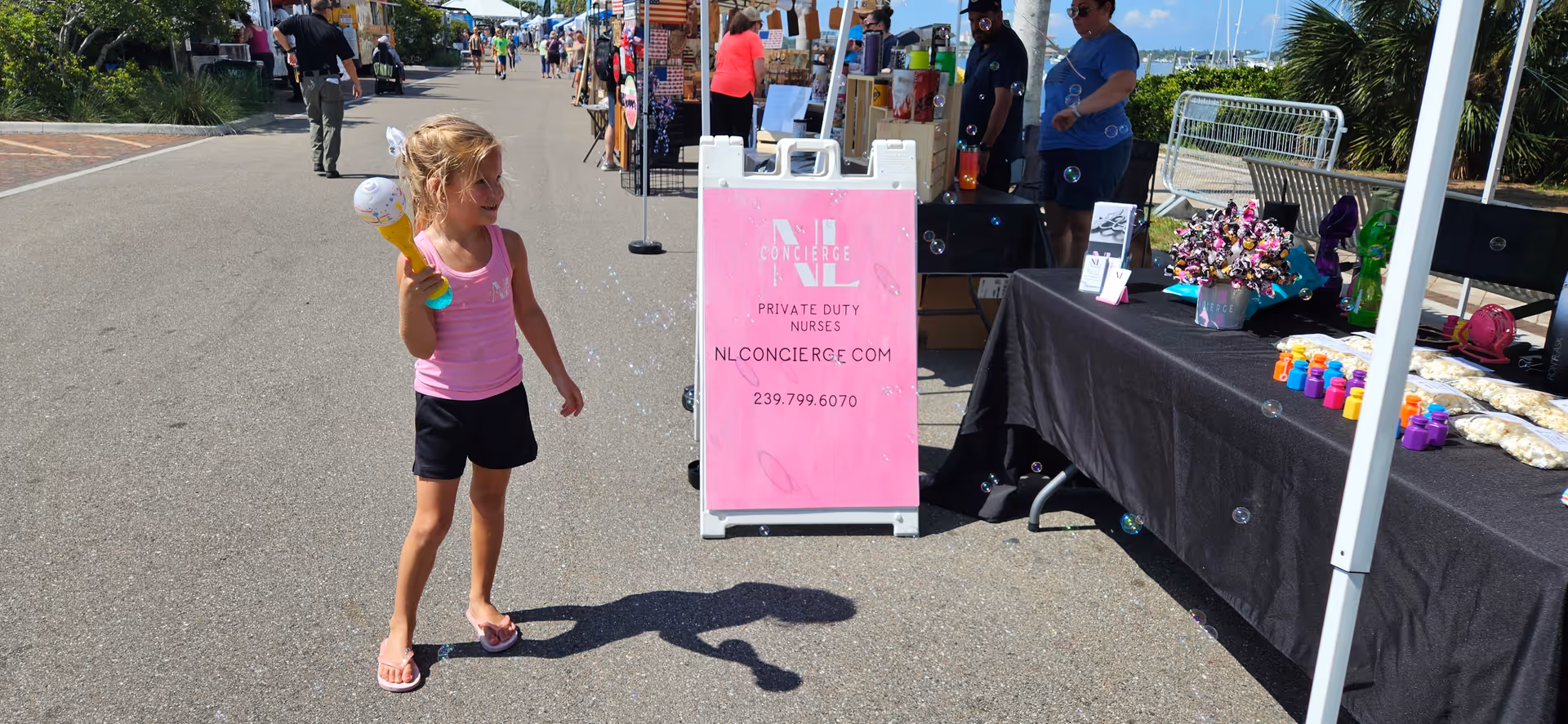 A young girl in pink holds an ice cream cone at an outdoor market.