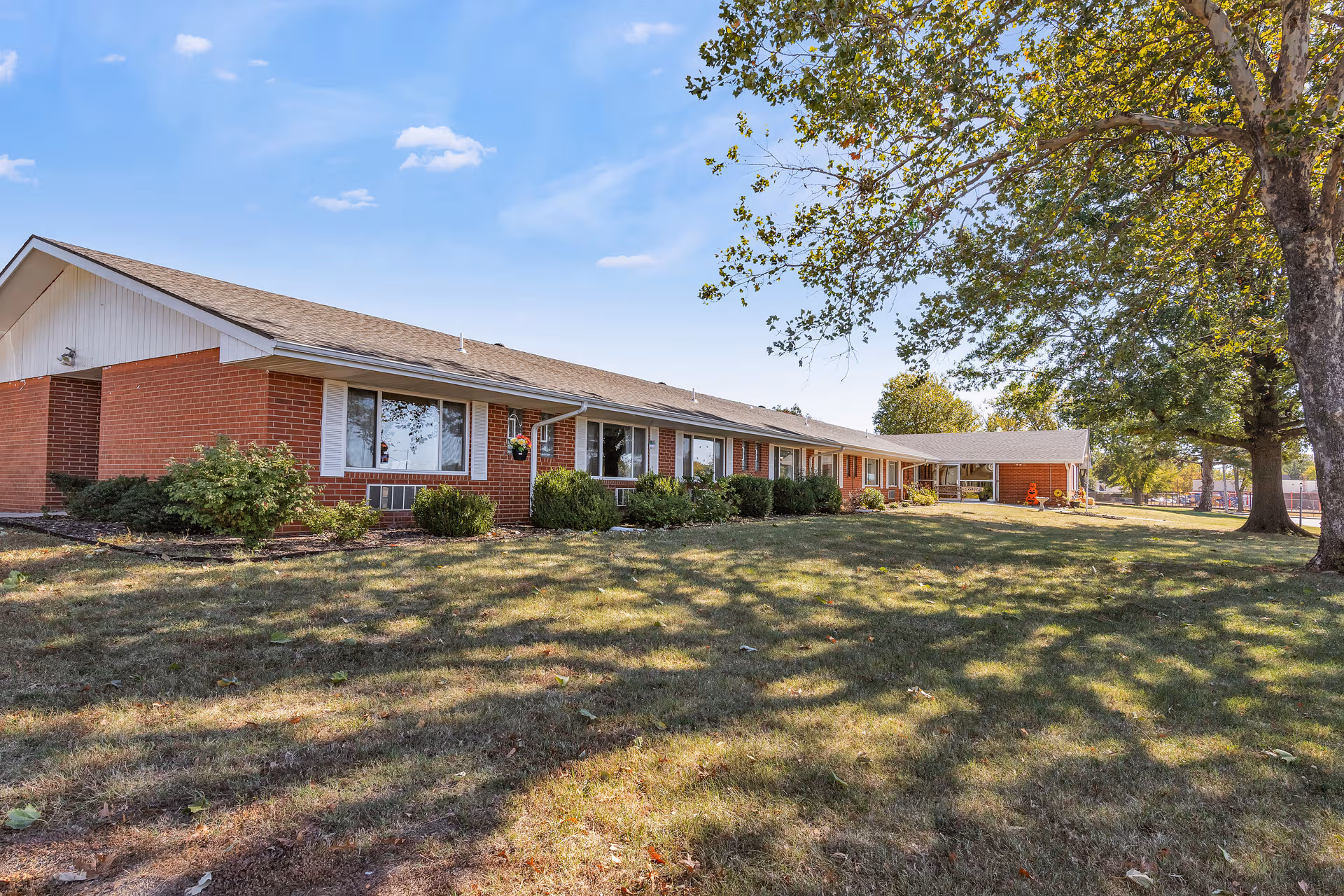 A single-story brick senior living center with a manicured lawn and trees.