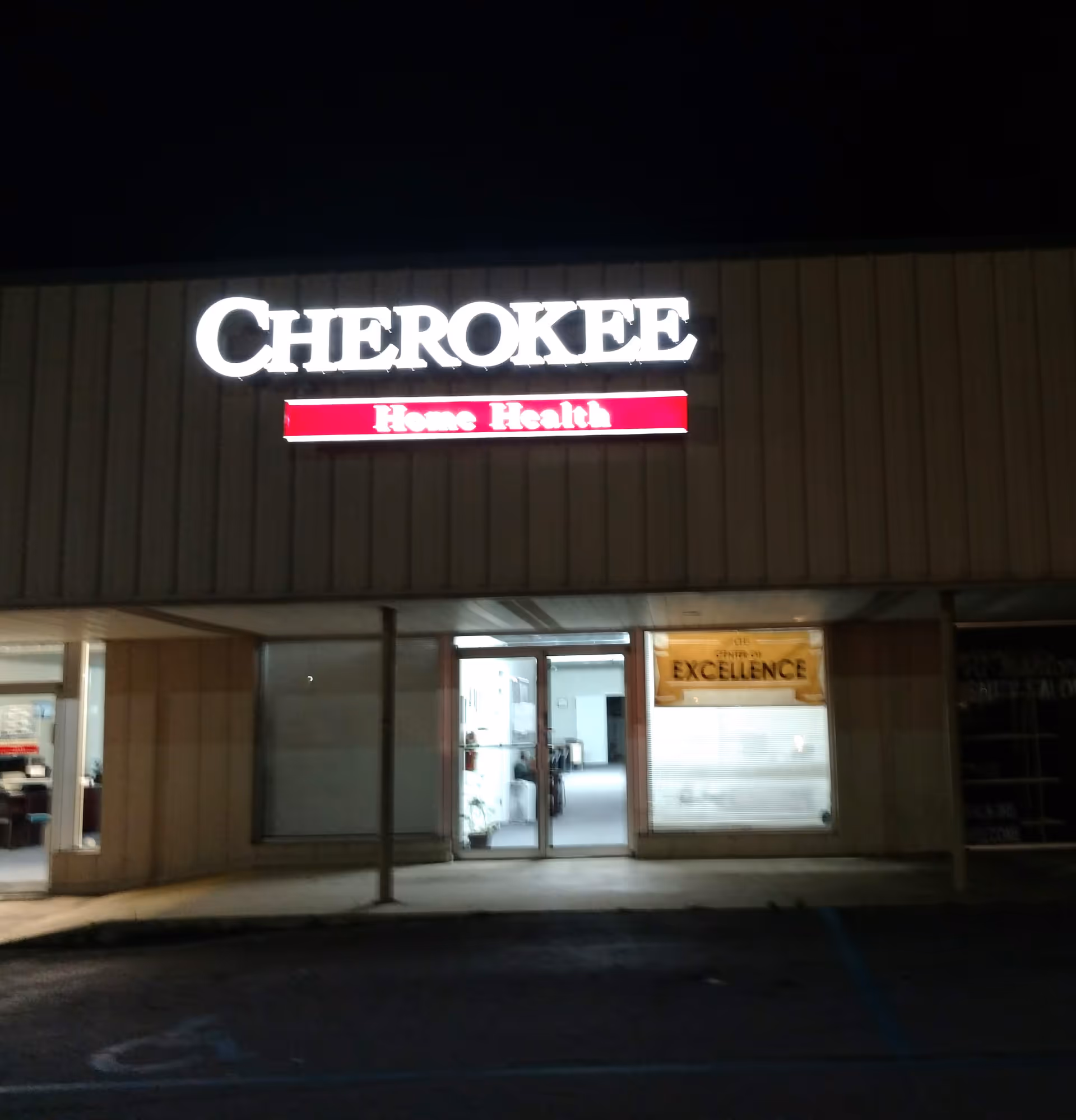 Night exterior of Cherokee Home Health building with illuminated sign and glass entrance.