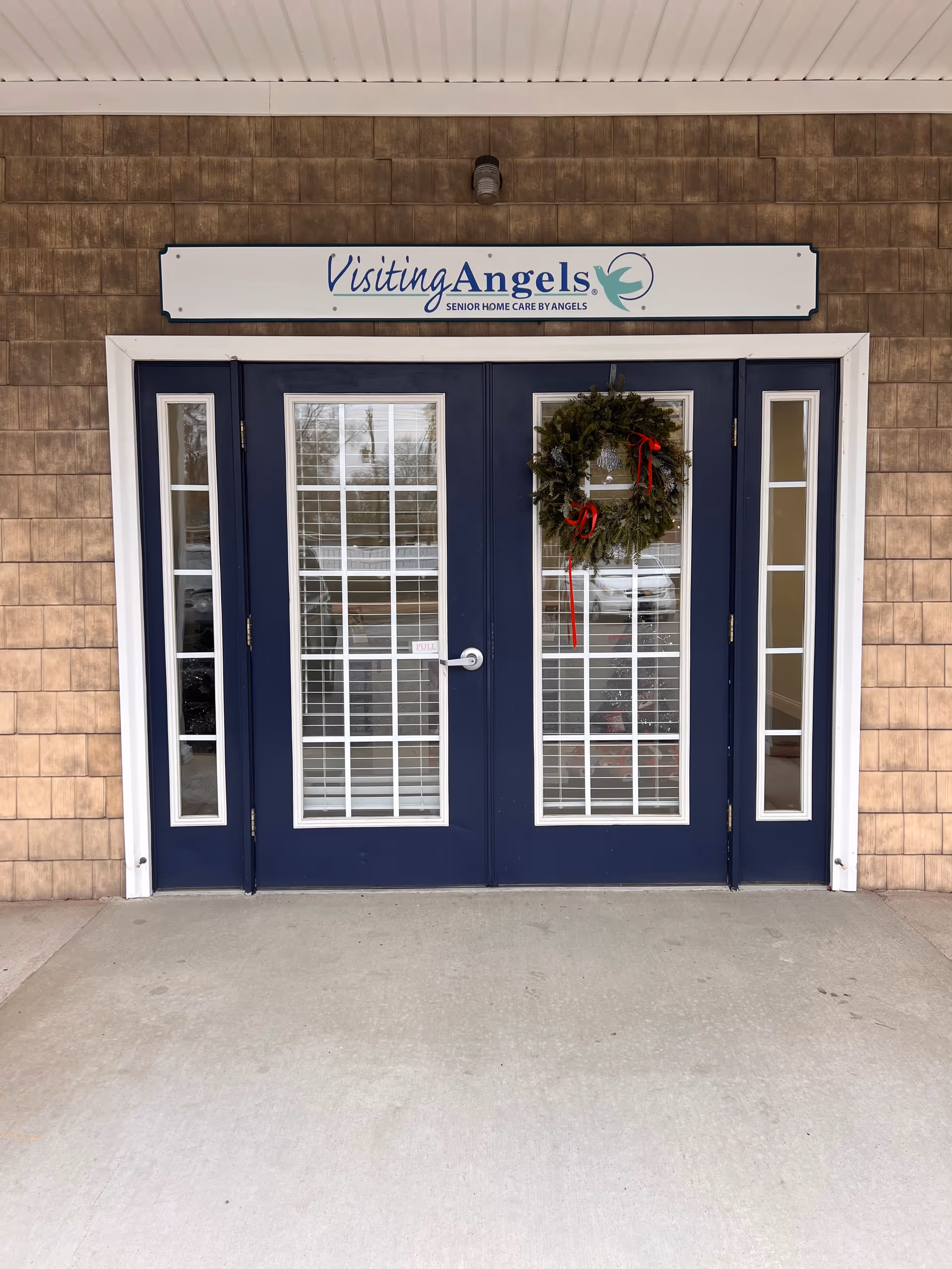 Double navy doors with glass panels and a wreath under a Visiting Angels sign.
