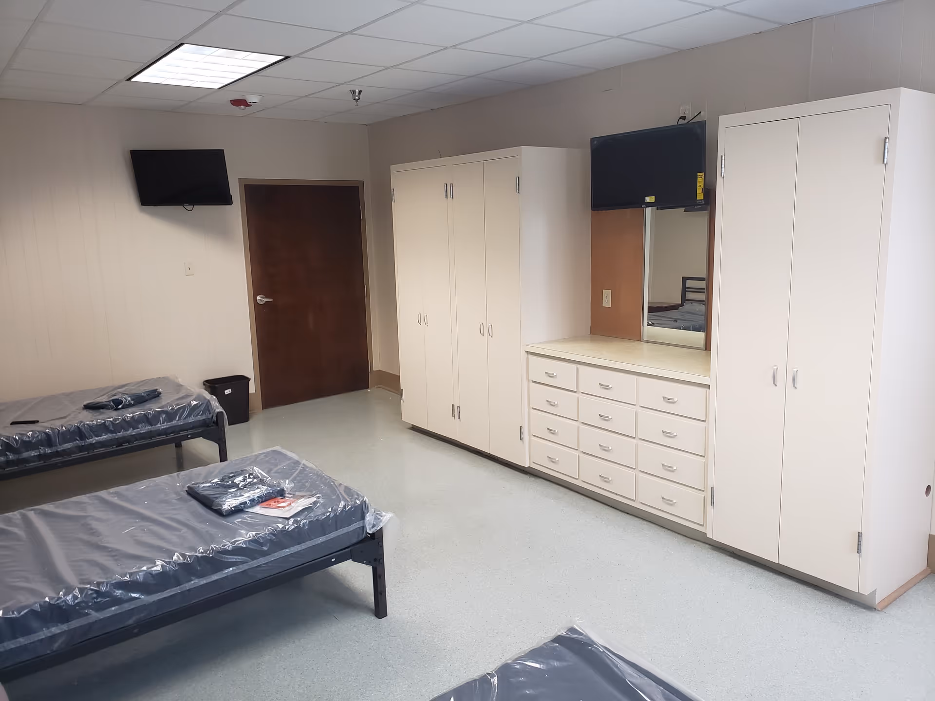 A clean shared bedroom with two single beds, white wardrobes, a dresser, and a wall TV.