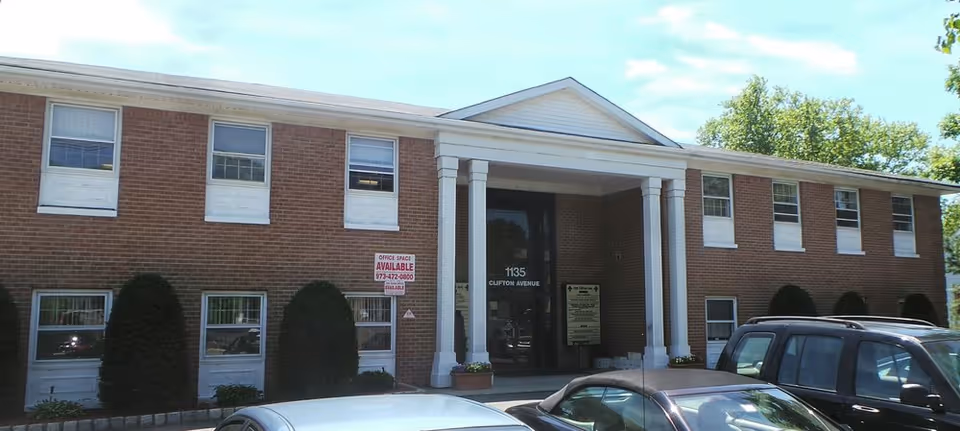 Exterior of a brick senior care facility with columns and parked cars.