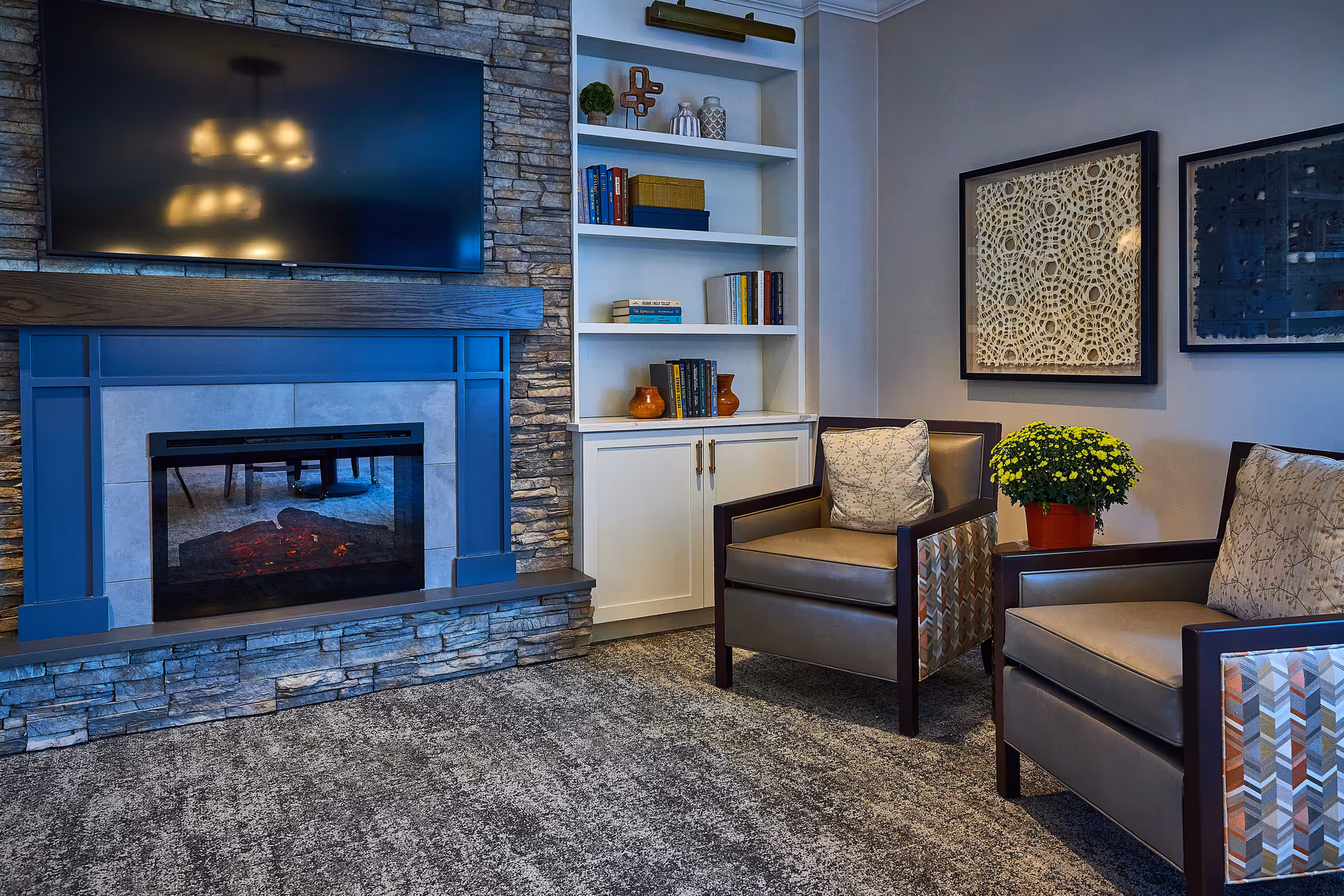 Cozy living room with stacked-stone fireplace, built-in shelves, TV, and two armchairs.