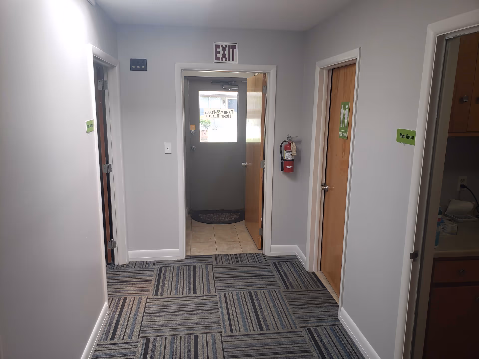 Interior hallway of a senior facility with doors, exit sign, and a fire extinguisher.