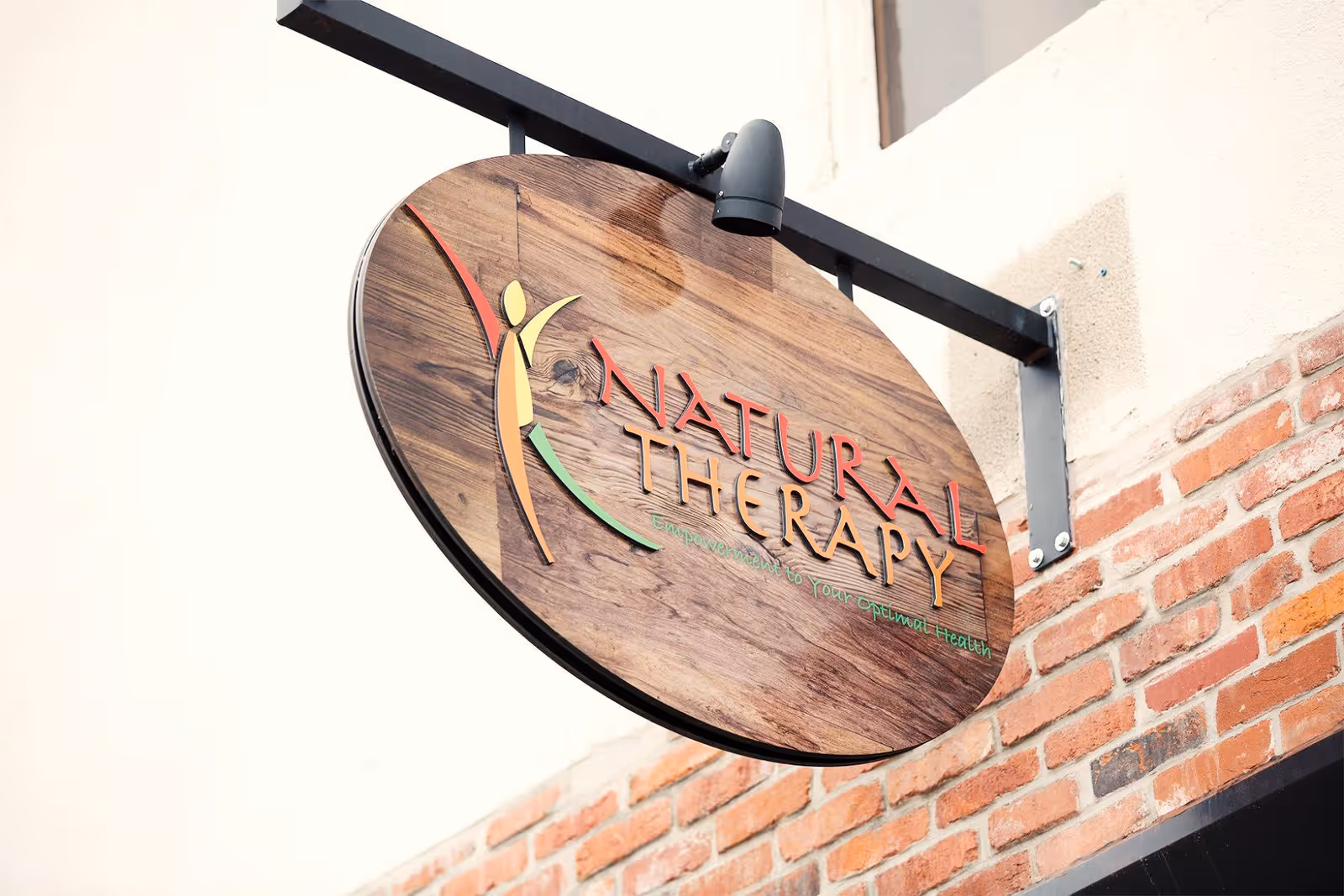 Round wooden sign reading Natural Therapy mounted on brick exterior of a building.