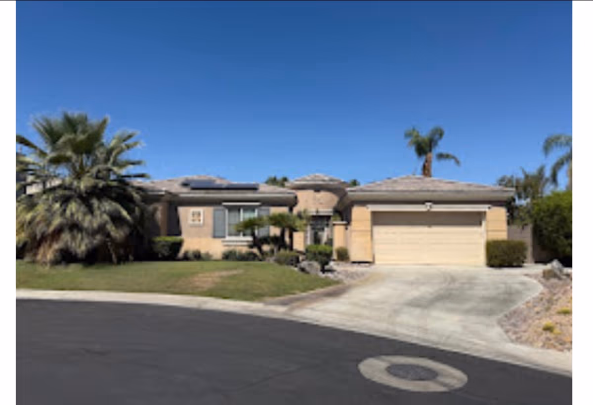 Single-story beige senior living facility with a curved driveway, palm trees, and a two-car garage.