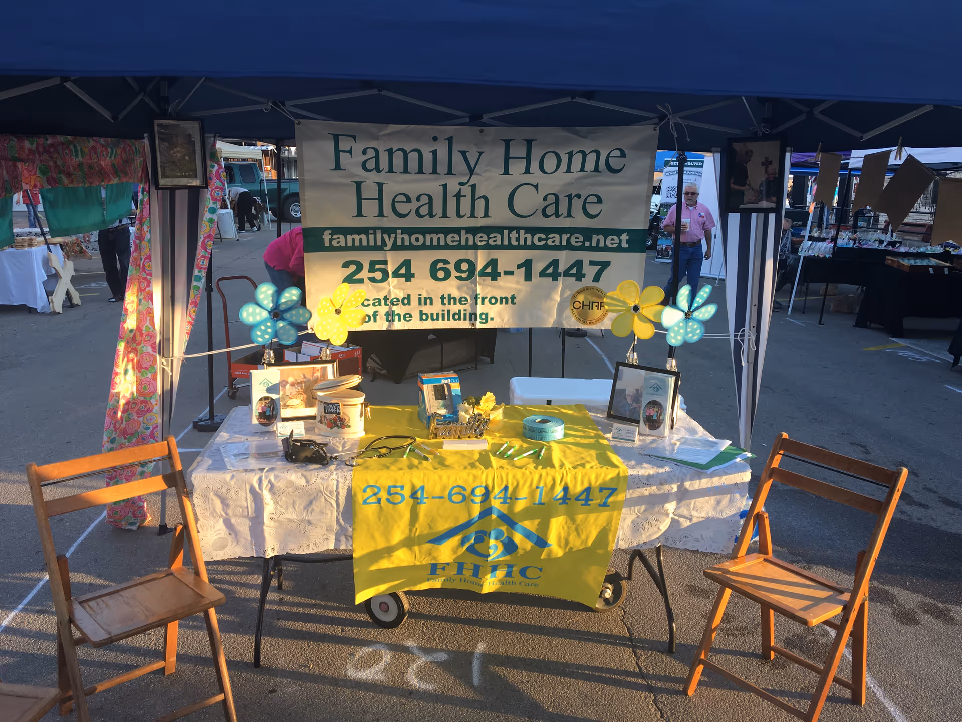 Outdoor tent booth displaying Family Home Health Care banner with table, chairs, and promotional items.