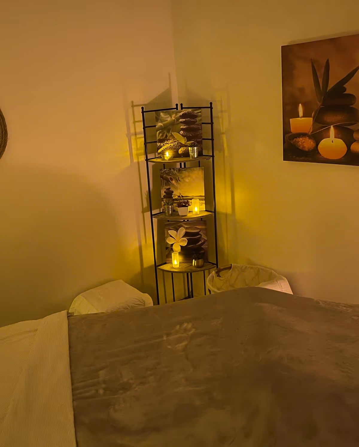 Dimly lit therapy room with a massage bed and decorative shelves with candles.