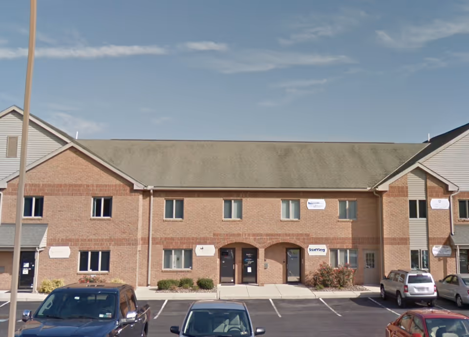 Brick senior living facility building with arches and parked cars in front.