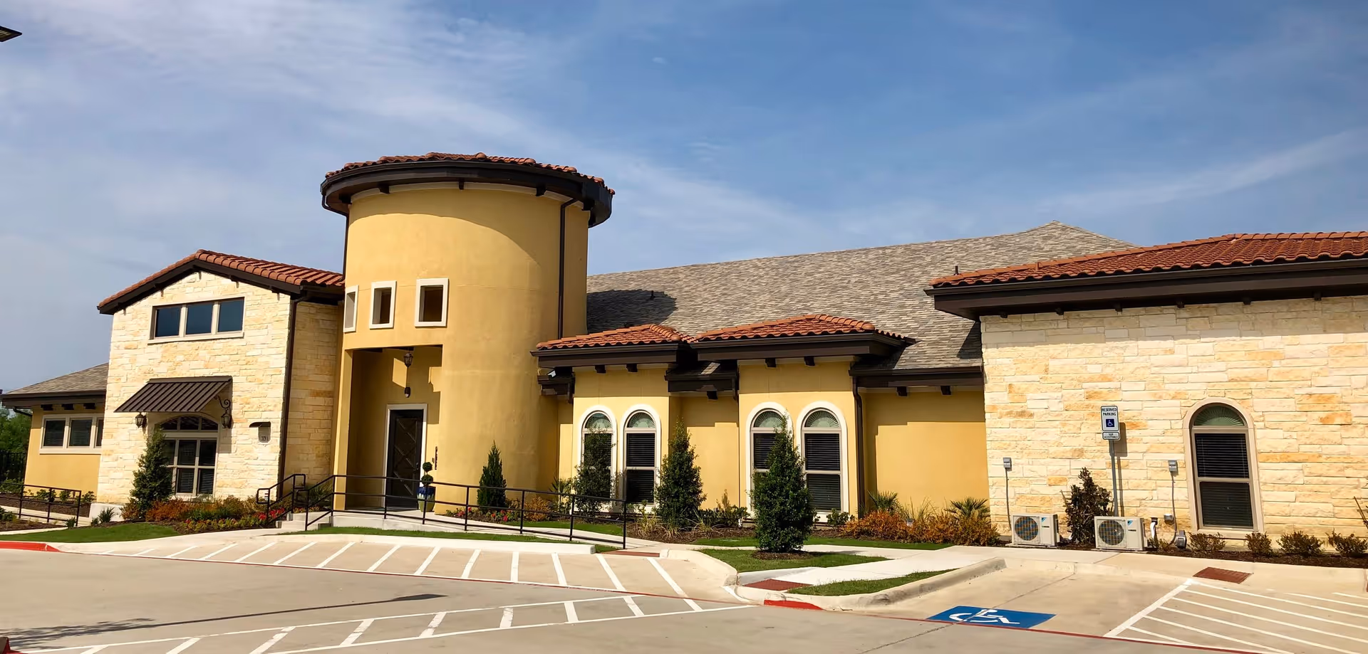 Exterior view of Windhaven Senior Living with tan stucco, stone accents, rounded tower, and parking.