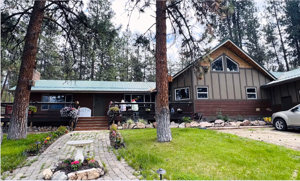 Single-story Mountain Pine Assisted Living Facility exterior with porch, trees, and landscaped front lawn.