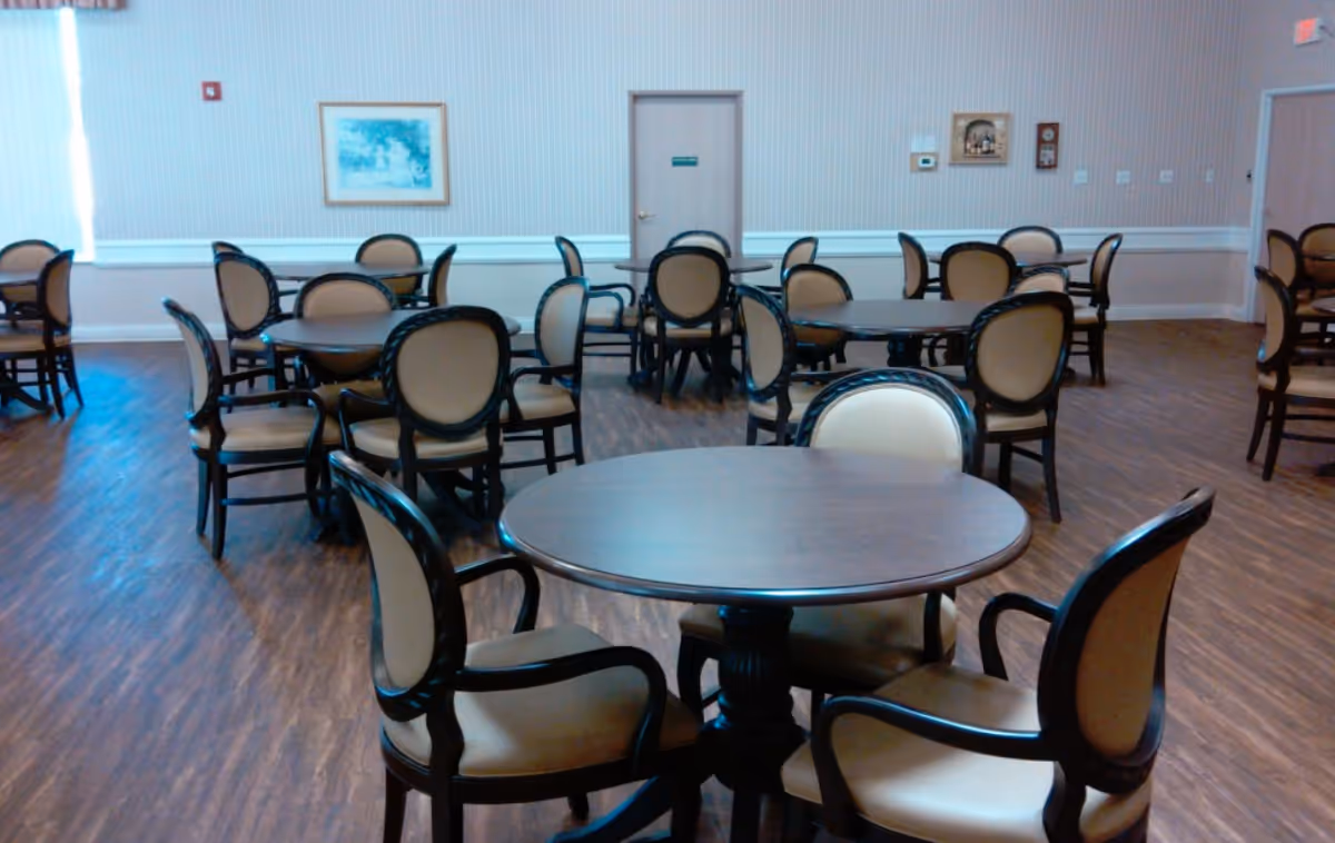 A spacious dining room with round tables and upholstered chairs at Calera Manor Nursing Home.