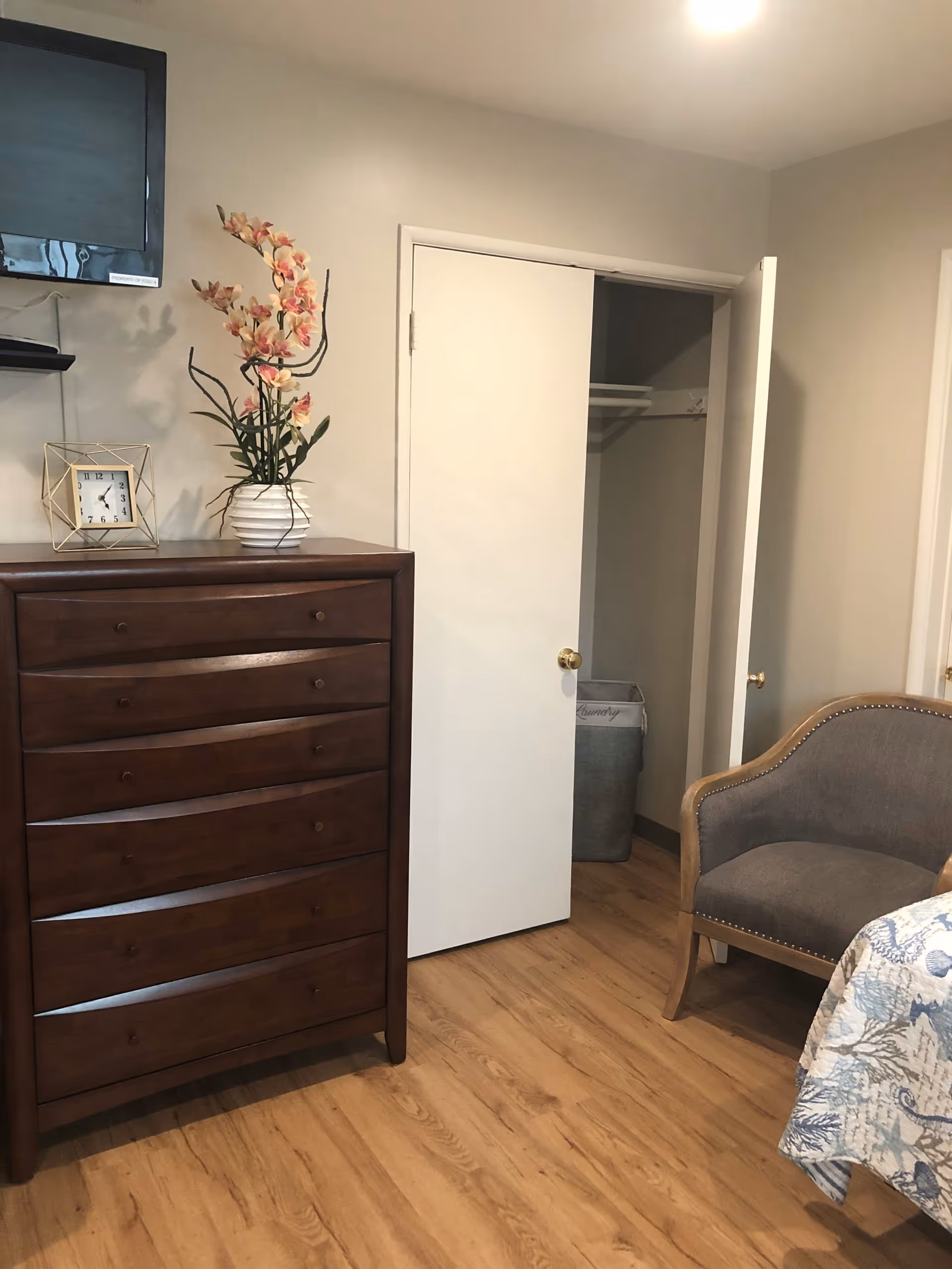 A cozy bedroom in a senior living room with dresser, chair, bed, and open closet.