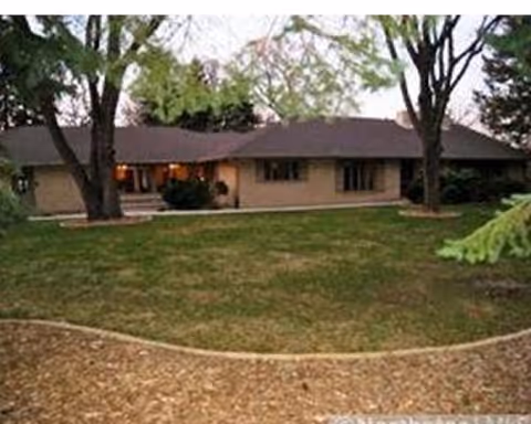 Single-story beige building with a front lawn, trees, and a curved gravel border.