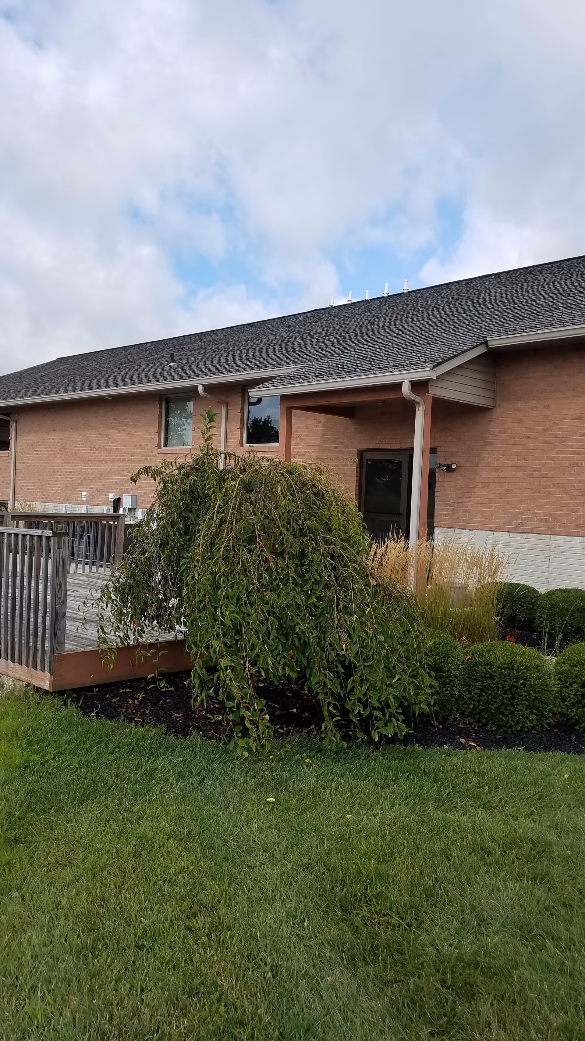 Exterior view of a brick senior living facility with a deck and landscaped lawn.