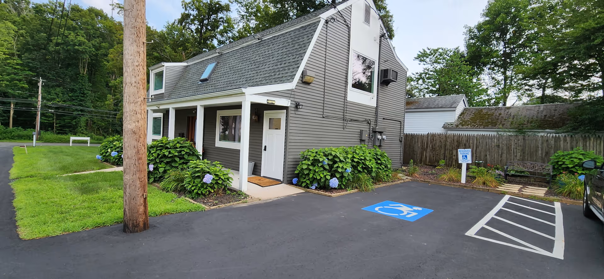 Small grey senior living facility exterior with accessible parking and greenery.