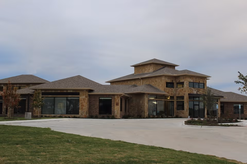 Stone-clad senior living facility exterior with large windows and a circular driveway.