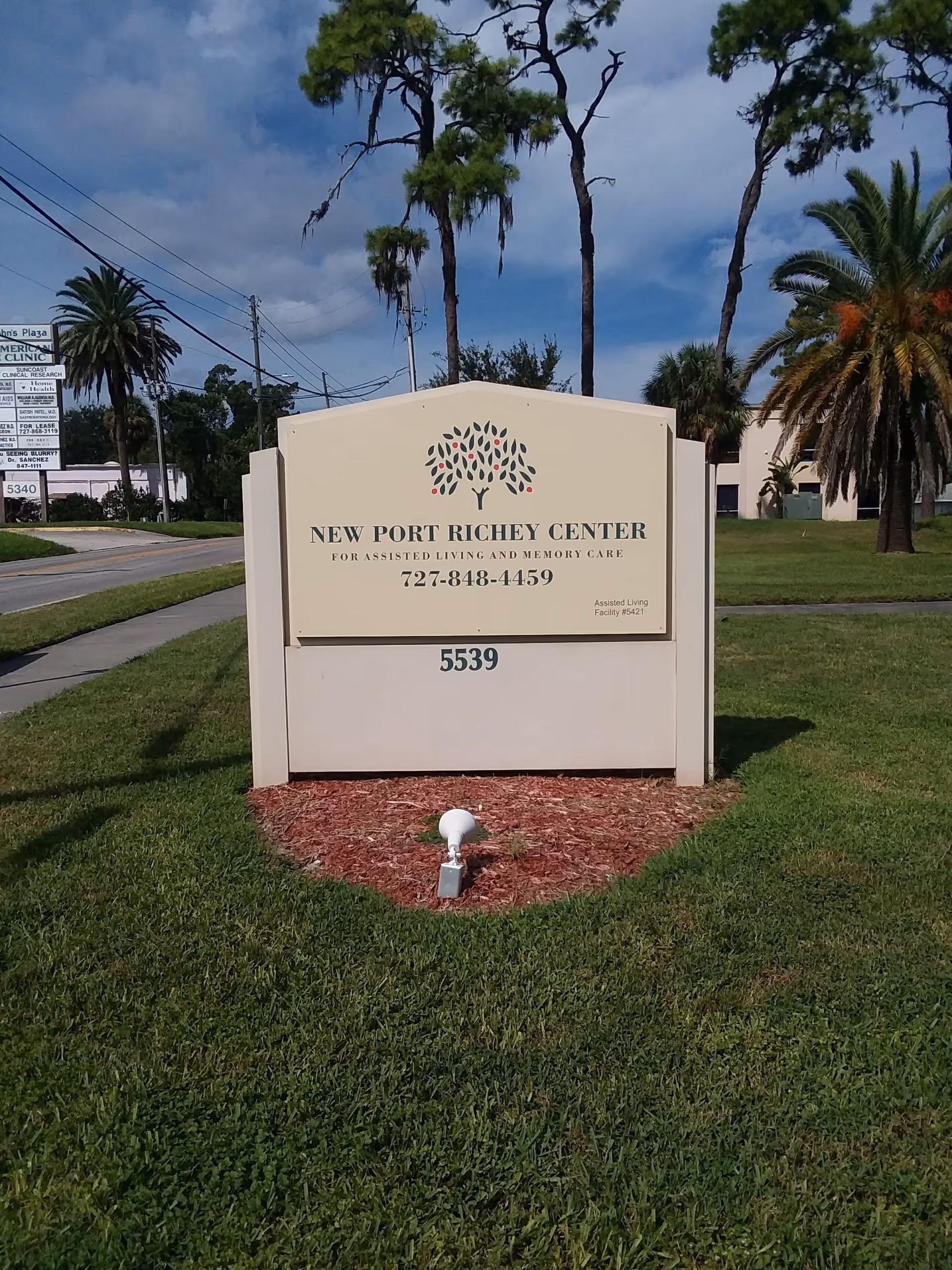 Exterior sign for New Port Richey Center on a grassy lawn with palm trees.