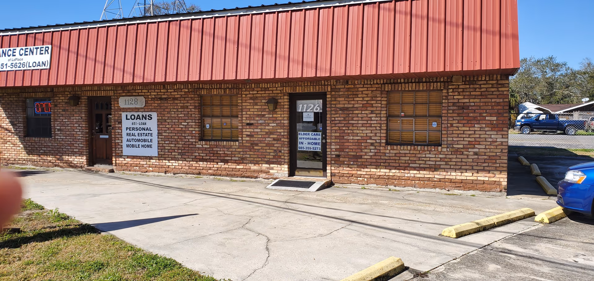 Brick storefront with a red metal awning and a front parking lot.