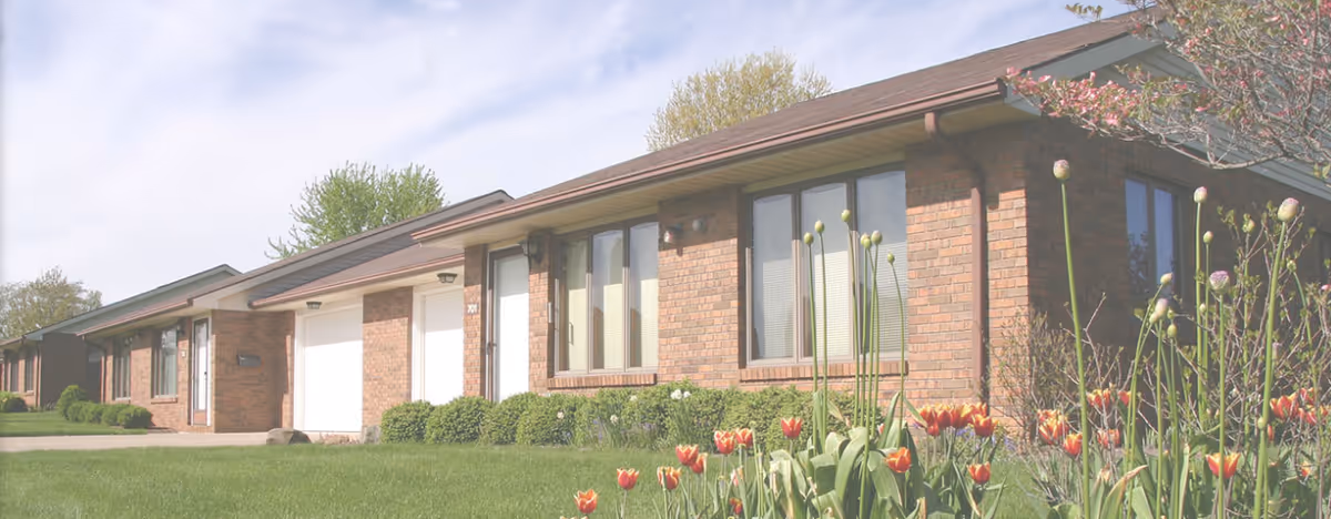 Single-story brick senior living building with manicured lawn and tulips in foreground.