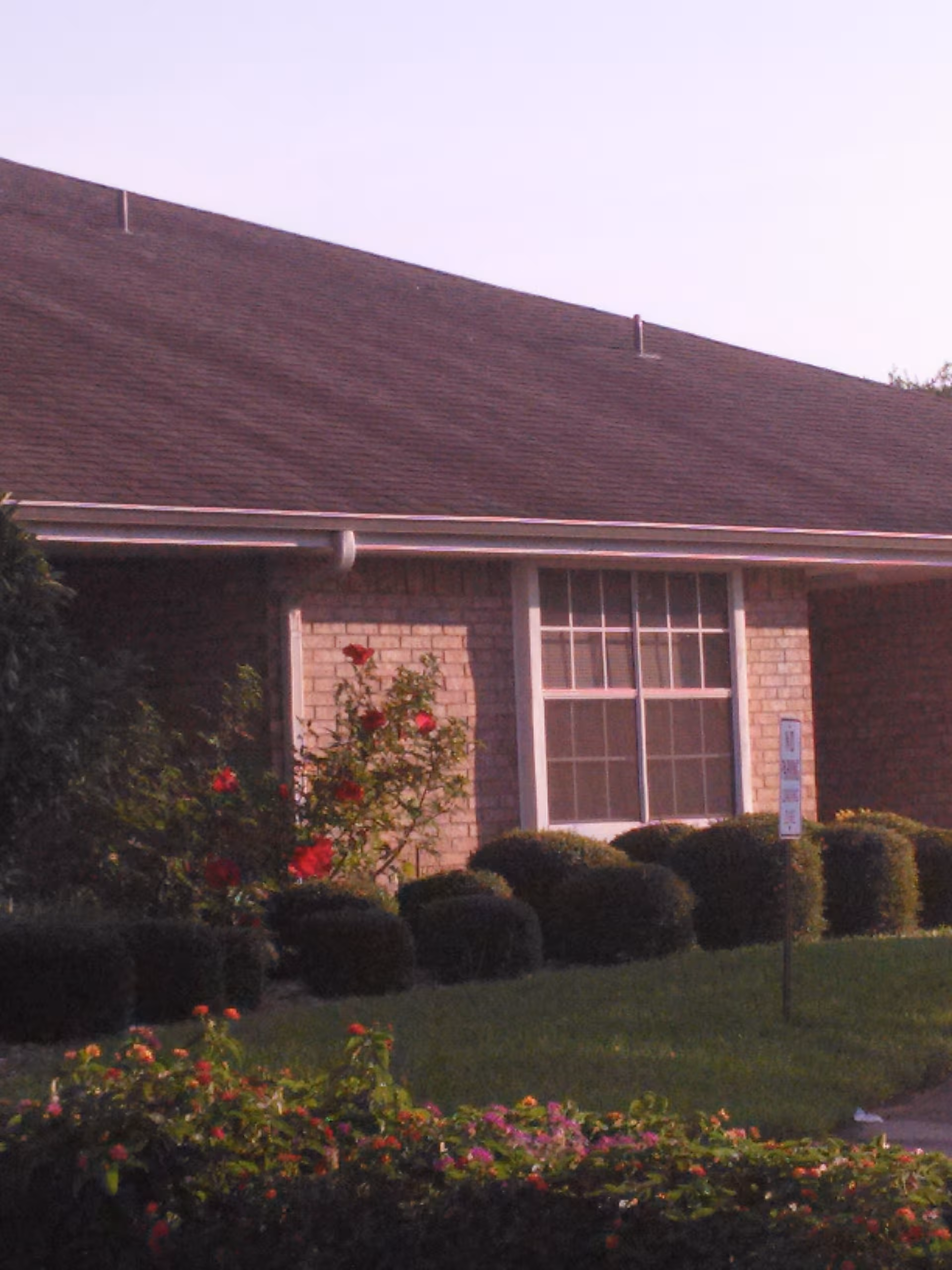 Exterior of a brick senior living facility with a large front window and manicured shrubs