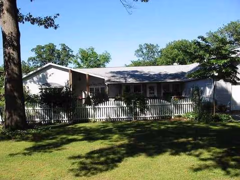 Single-story white house with a front porch, fence, and grassy yard.