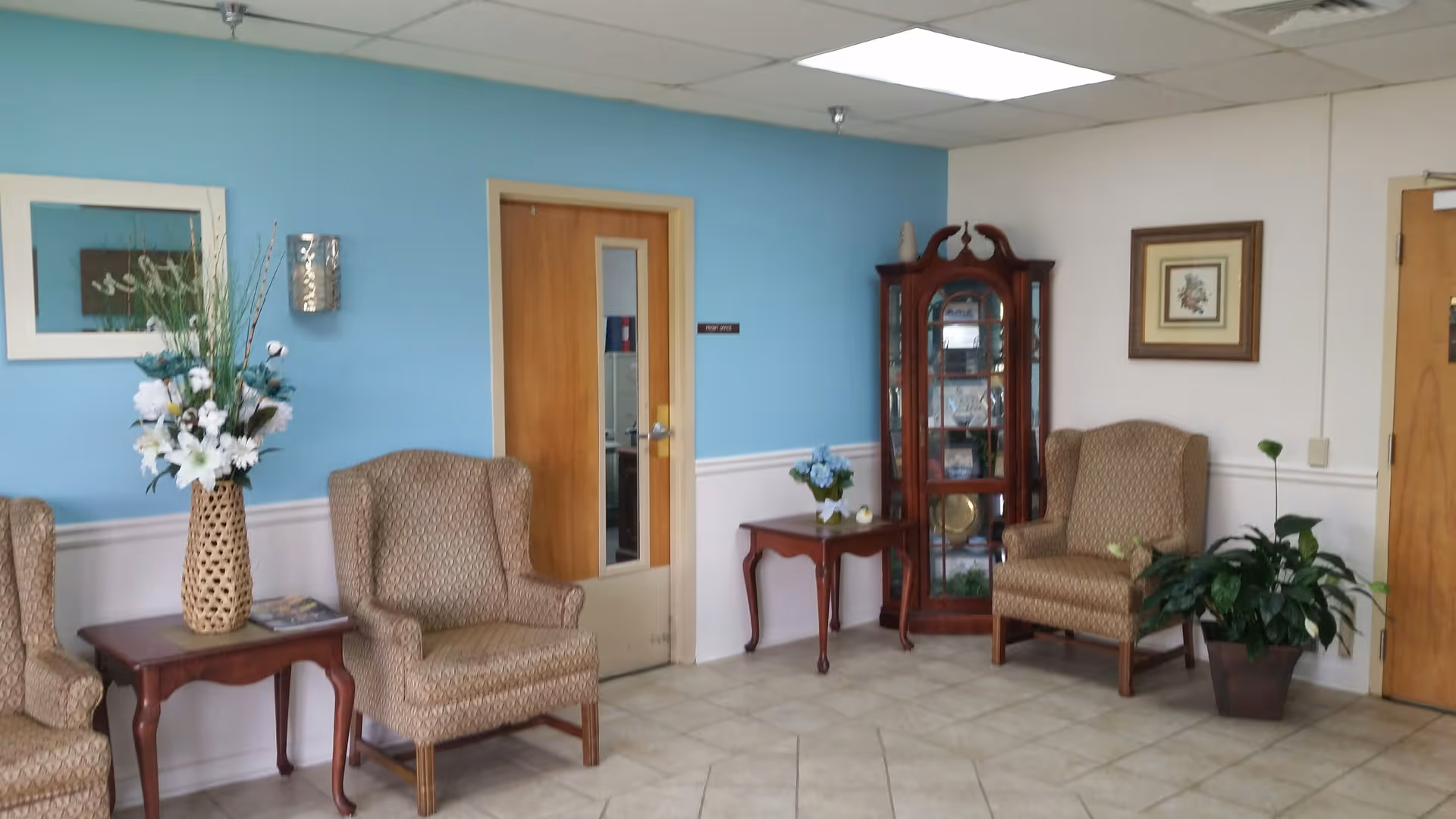 Bright lobby seating area with upholstered chairs, plants, and a glass display cabinet.