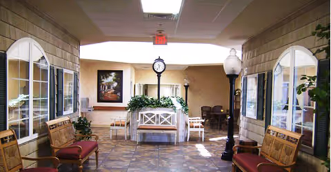 An empty senior living facility lobby with benches, clock, plants, and decorative lighting.