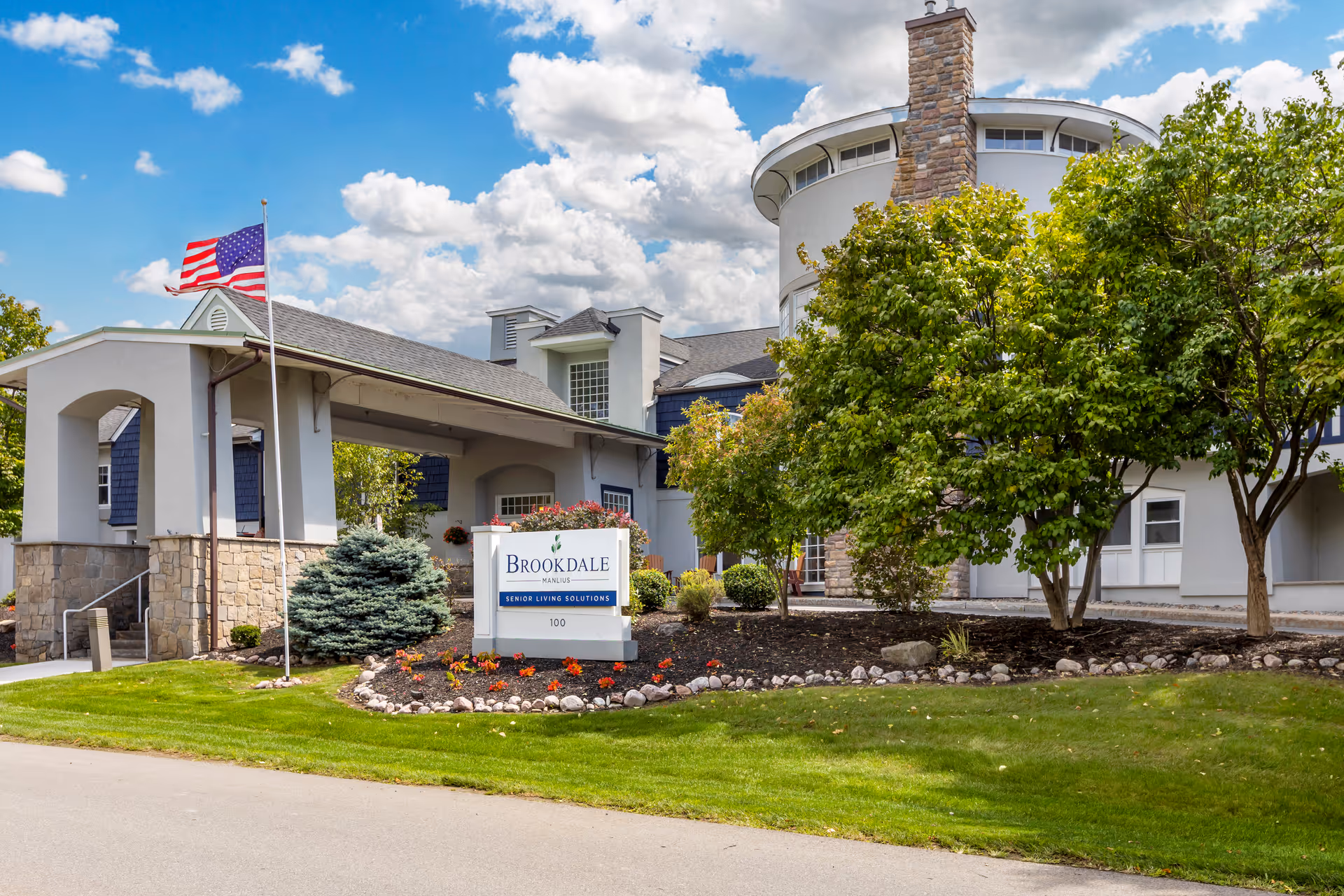 Exterior view of Brookdale Manlius senior living facility with sign, flag, and landscaped entrance.