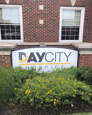 Brick building exterior with Day City Hospice sign and yellow flowers in front.