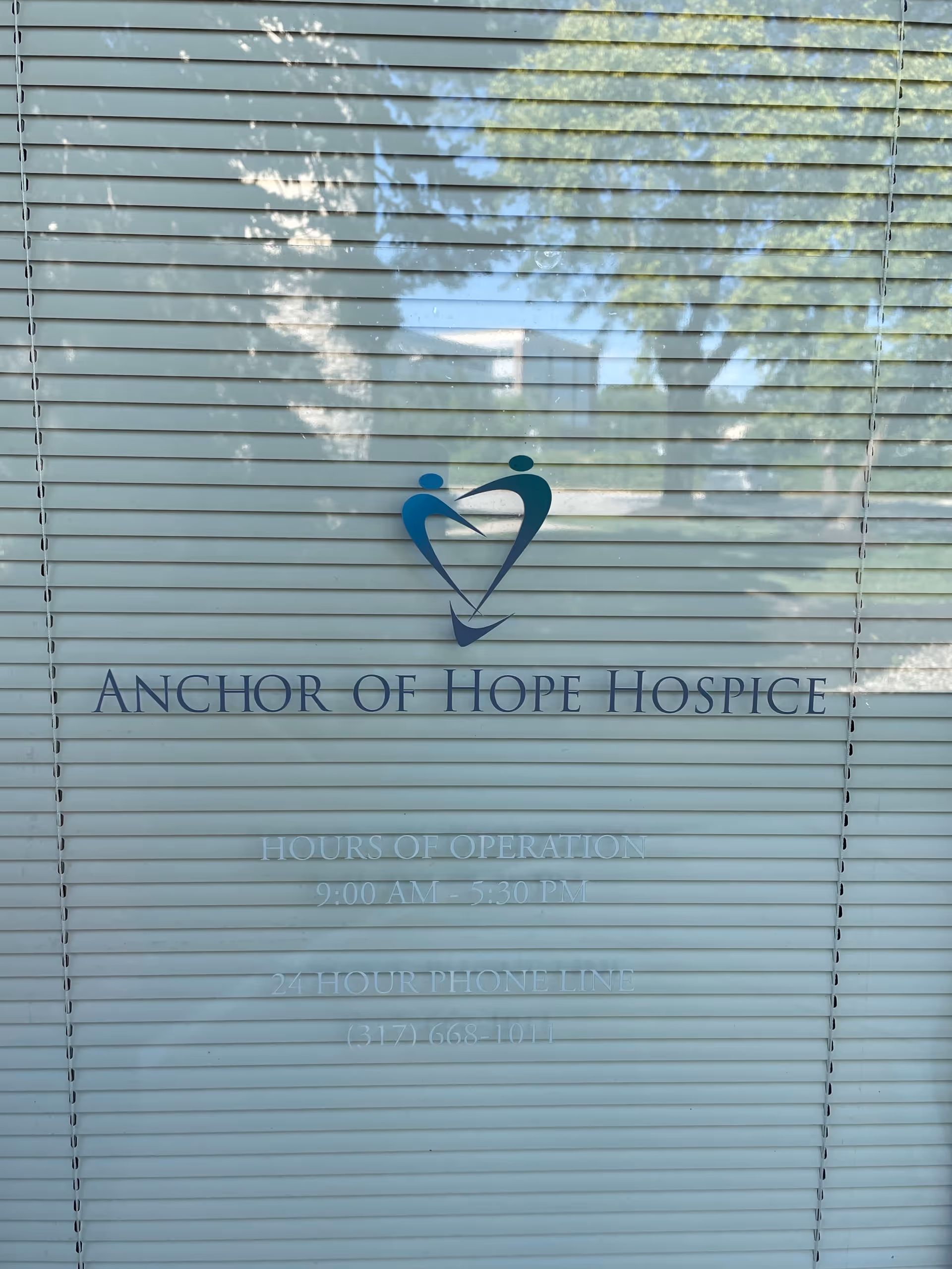Glass window with Anchor of Hope Hospice logo and hours on blinds.