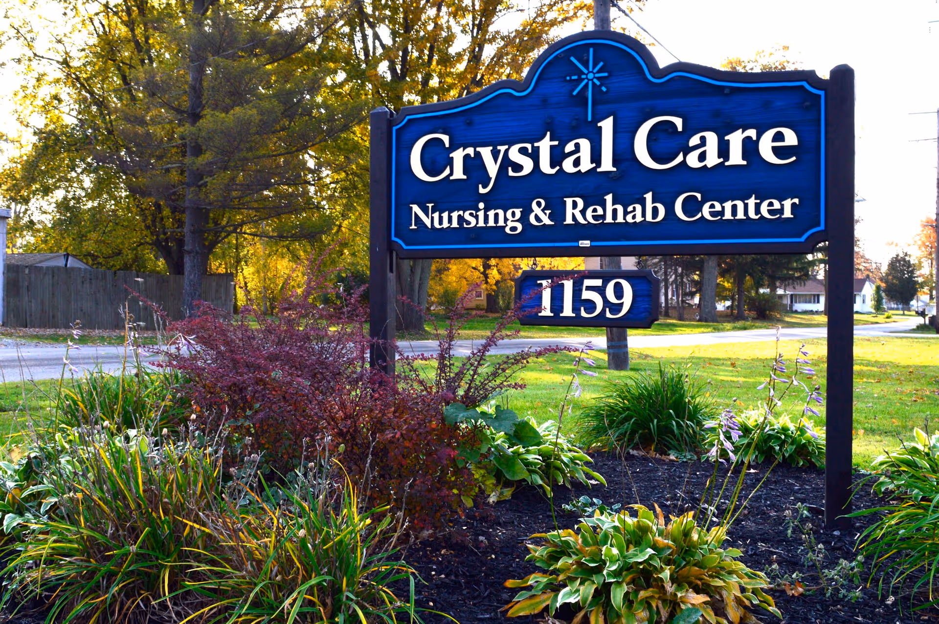 Exterior view of Crystal Care Nursing & Rehab Center sign among landscaped plants.