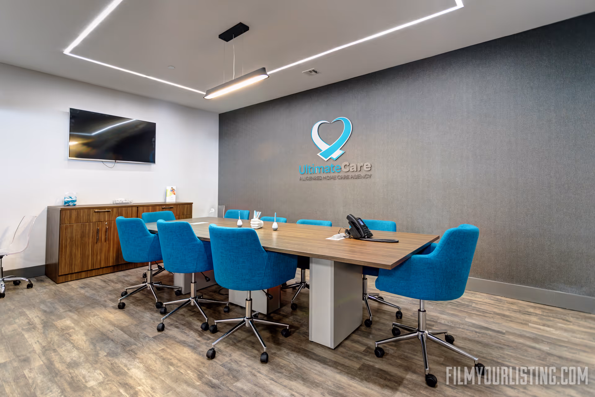 Modern conference room with blue chairs around a long table and Ultimate Care logo on wall.
