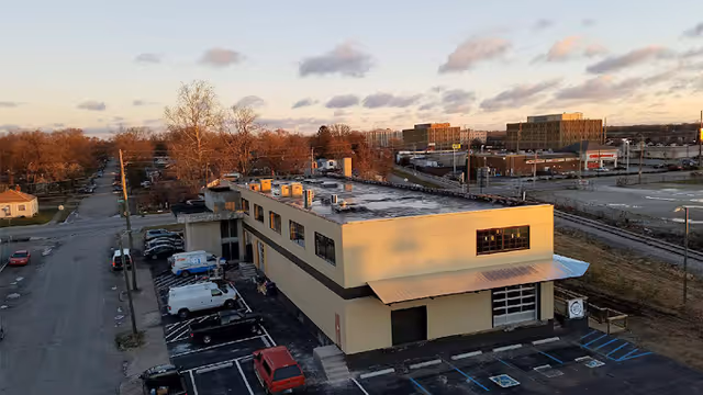 Exterior view of a beige two-story building with a parking lot and railroad tracks nearby.